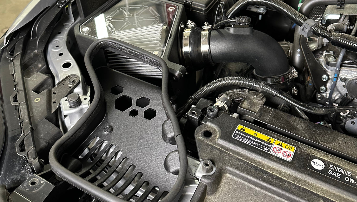 The image shows the black complete intake system installed under the hood of a vehicle, consisting of a airbox, intake tube and the area around the MAF sensor.